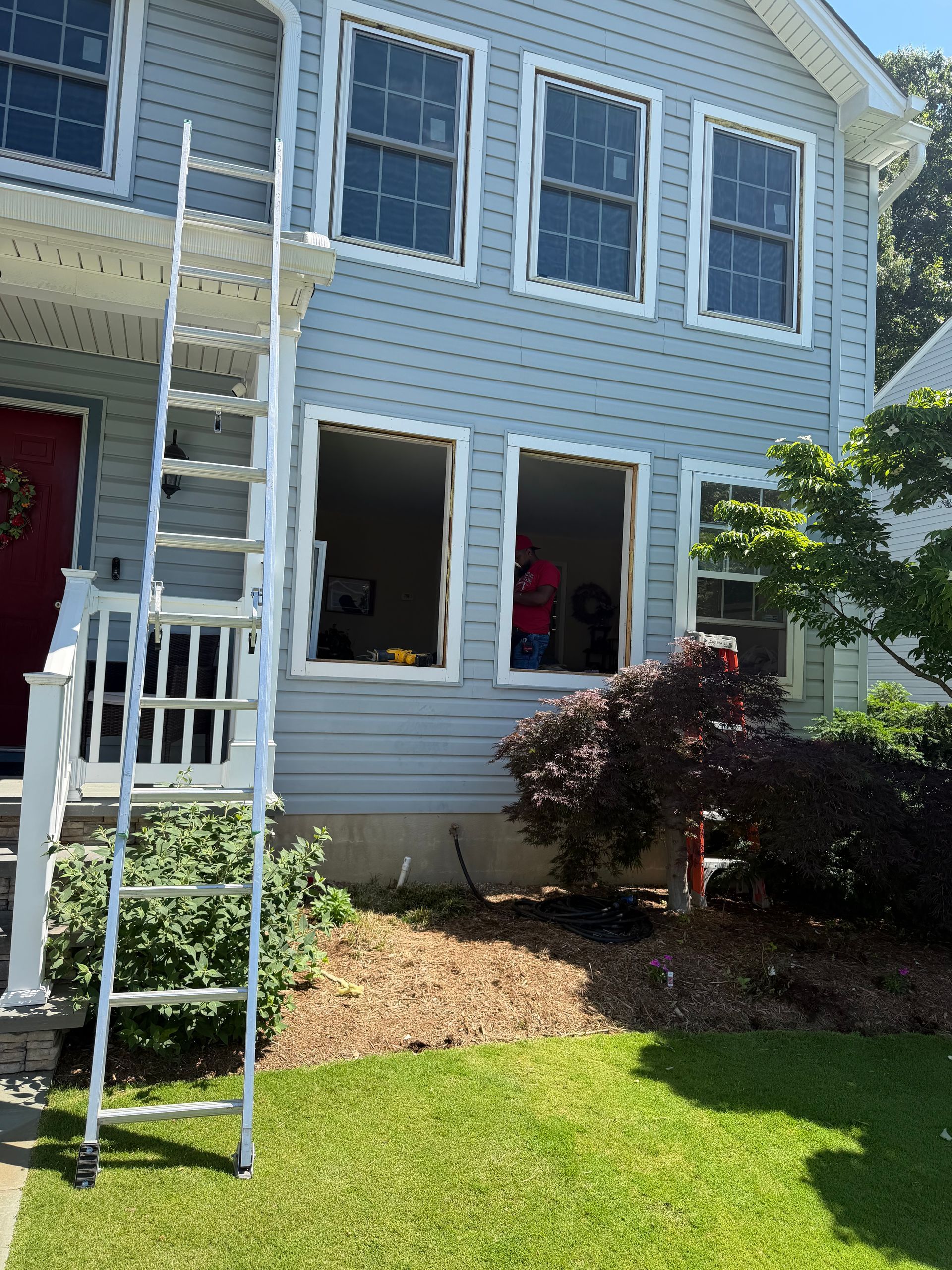 Two-story blue house with open windows, a white ladder, and a red front door.