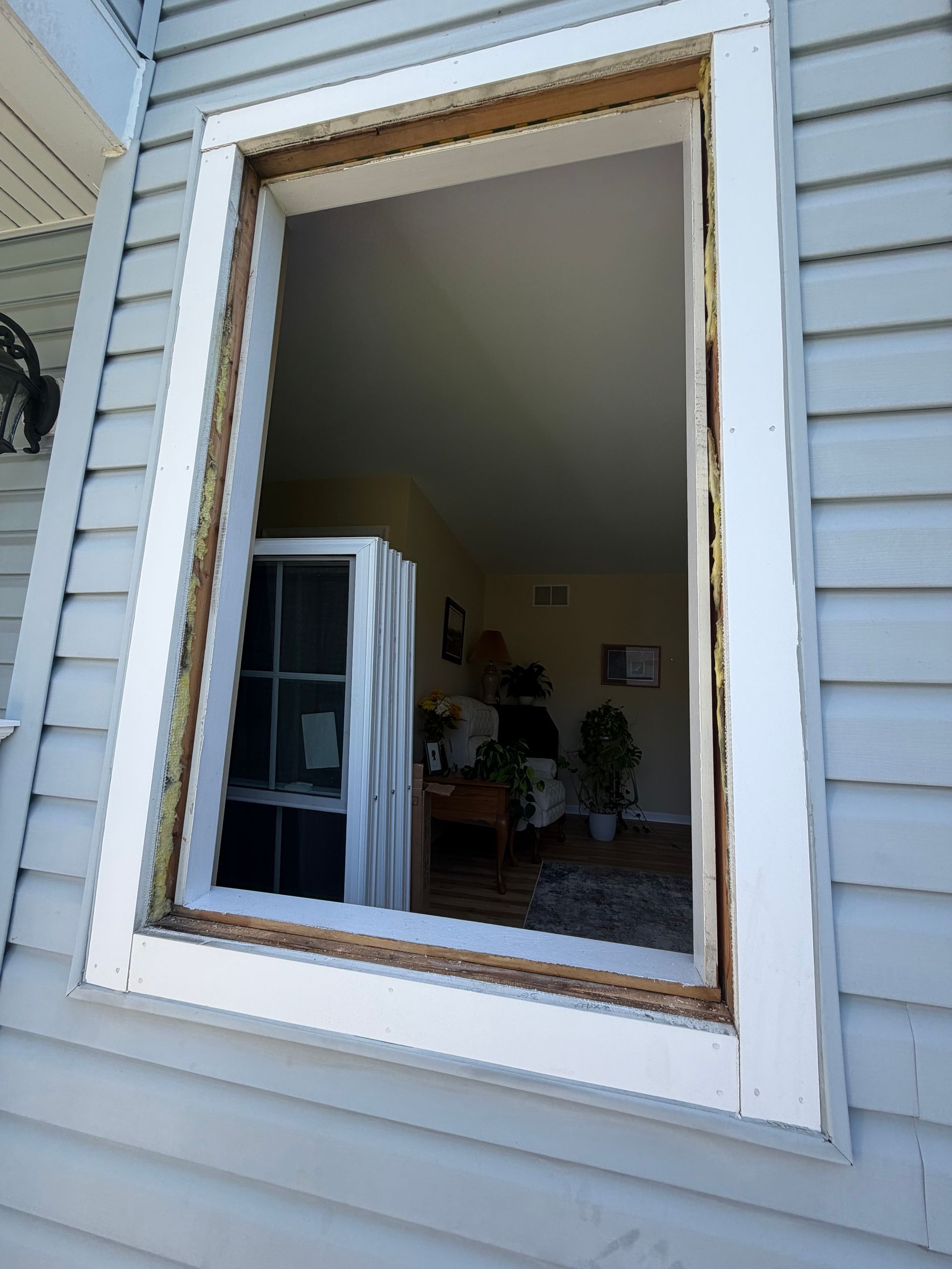 Open window with a view into a room, showing blue siding and white trim