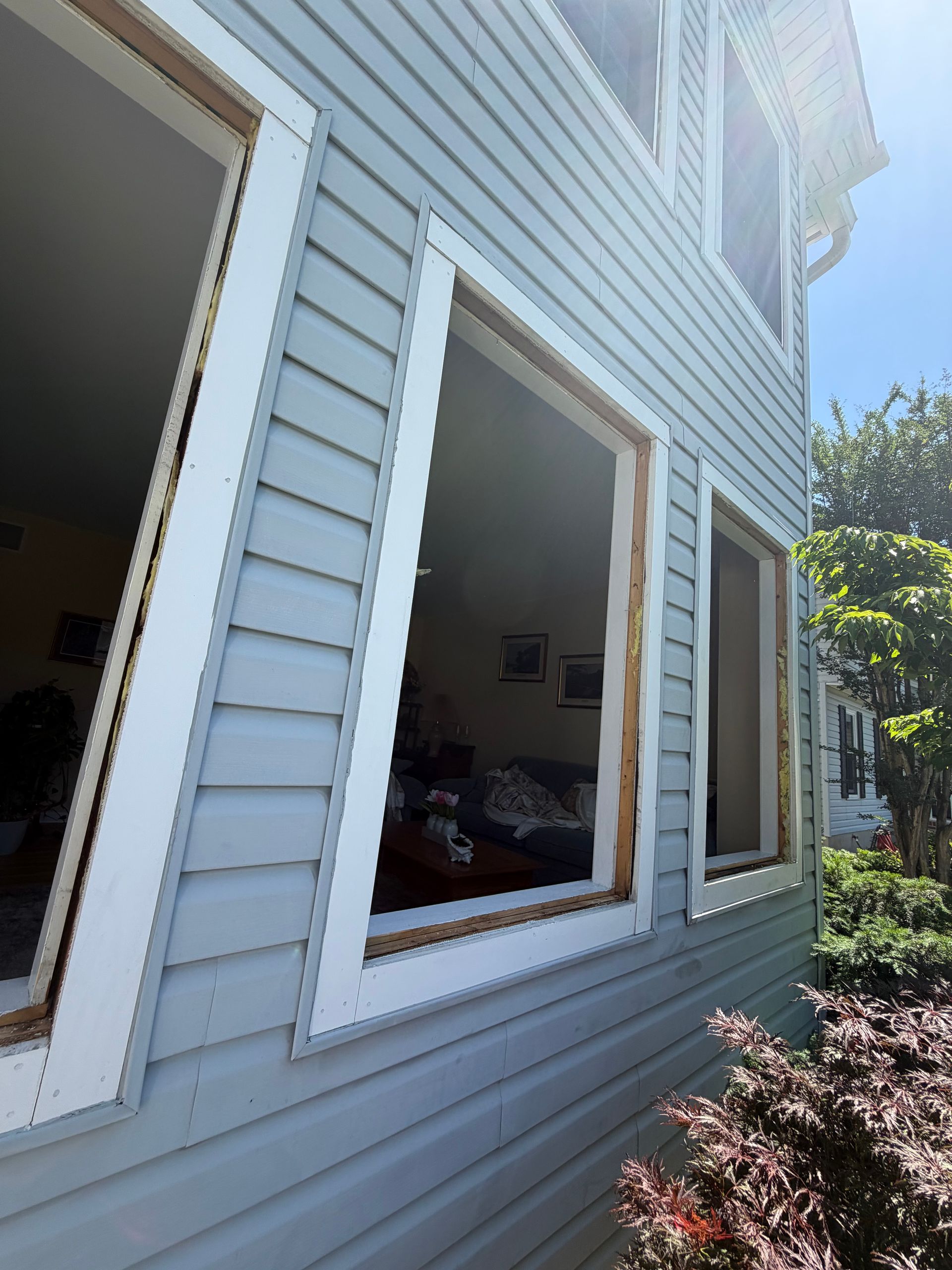 White house exterior with open windows, blue siding, and shrubs beside the wall.