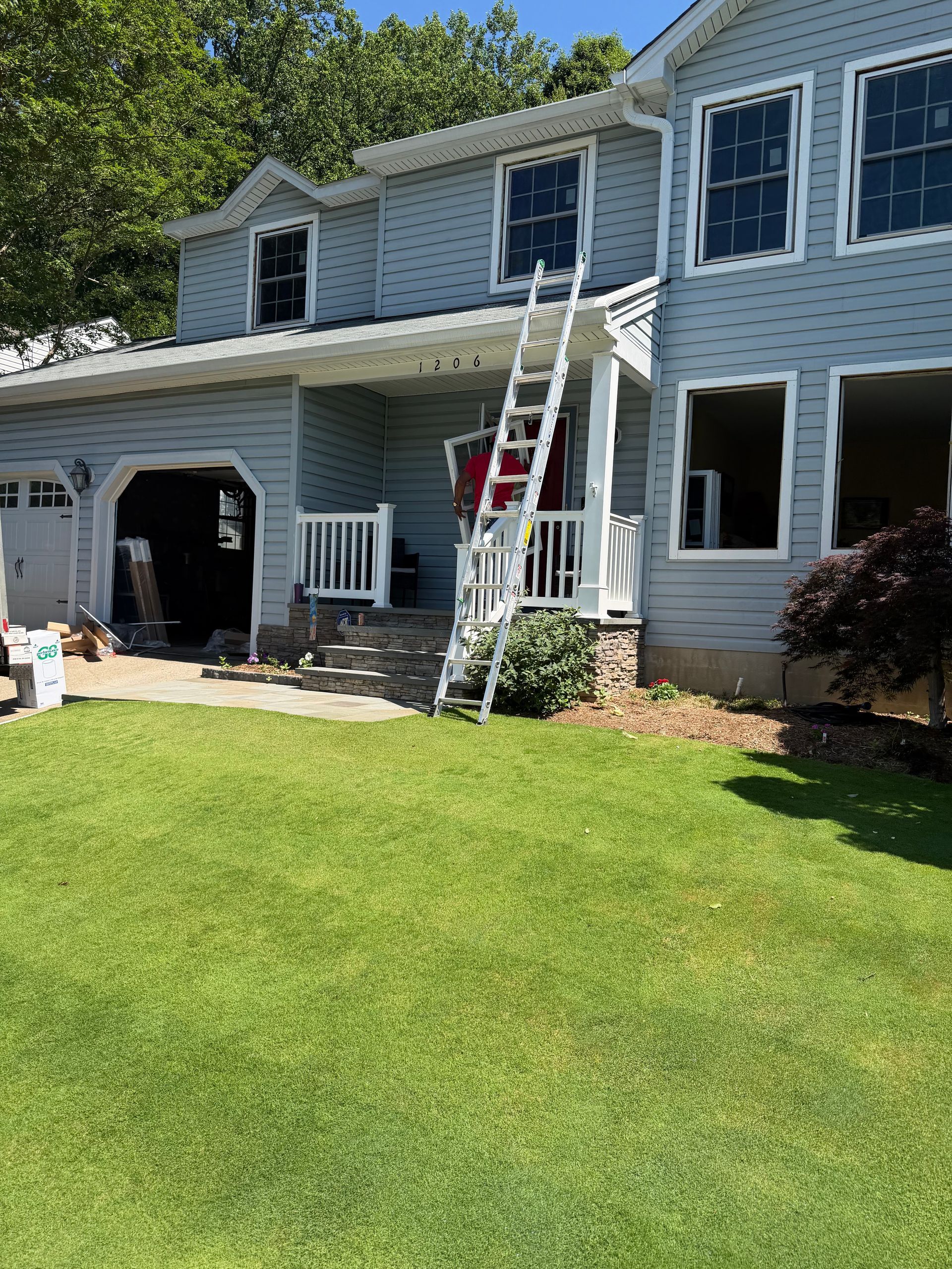 Worker on ladder painting a two-story blue house with white trim and a green lawn.