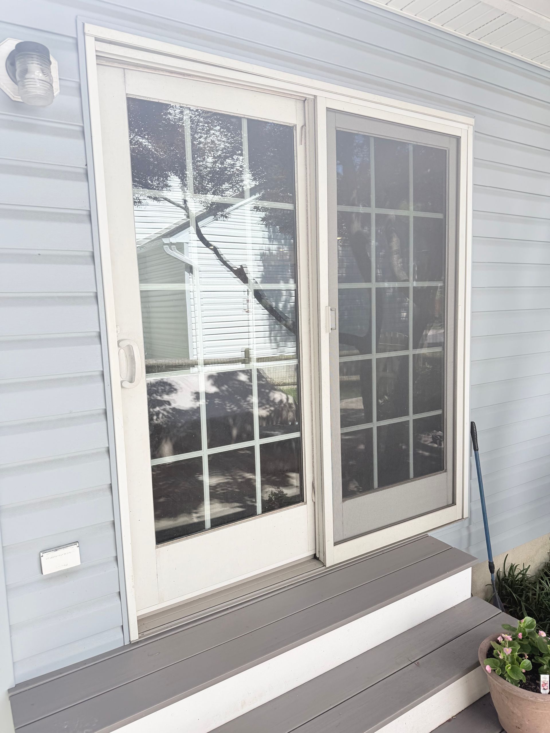White exterior sliding glass door with screen, small porch, and potted flowers beside it