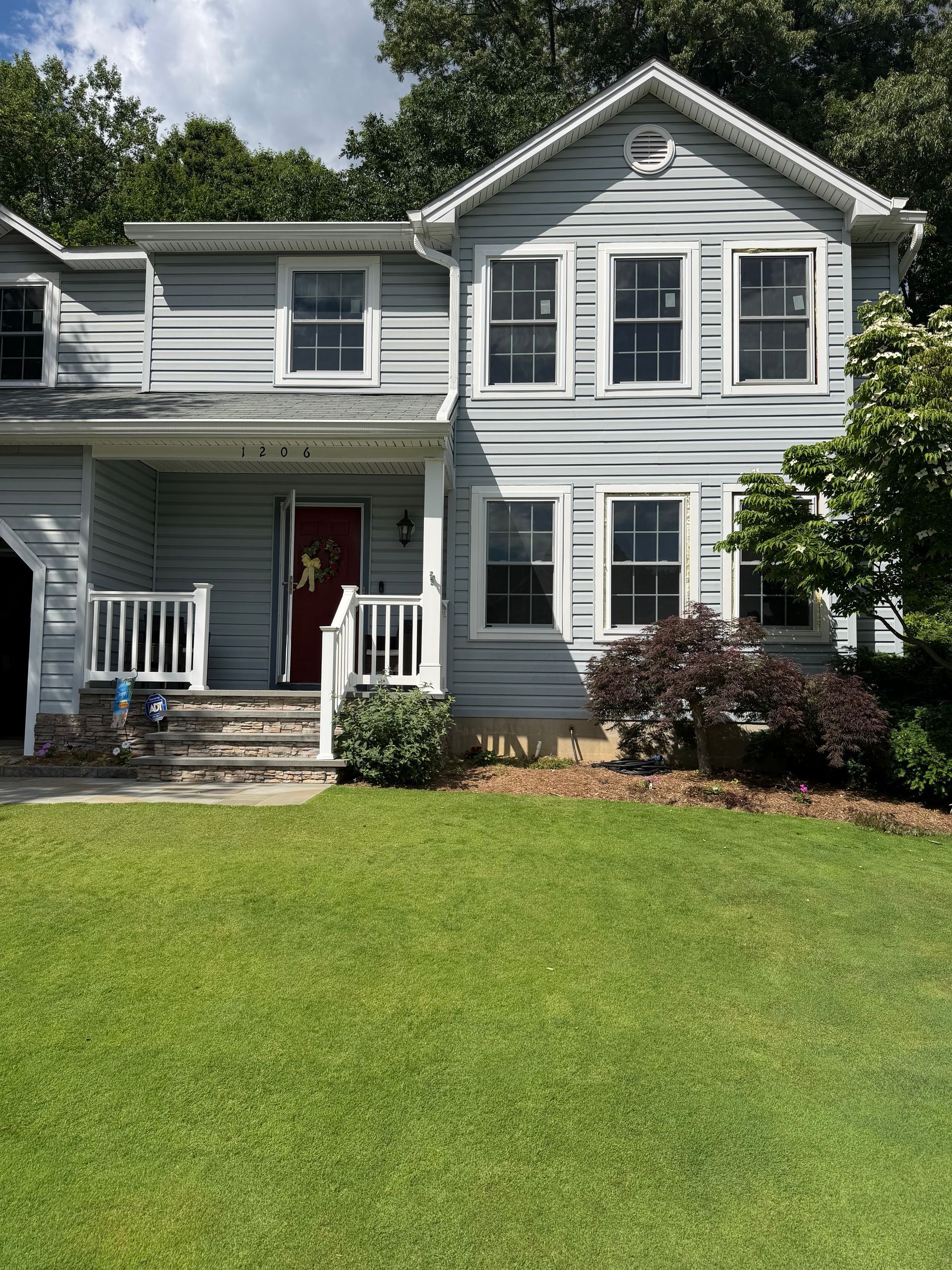 Gray two-story house with white trim, red front door, and a green lawn in front