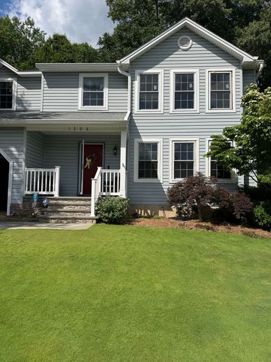 Two-story gray house with white trim, red front door, and green lawn under cloudy sky