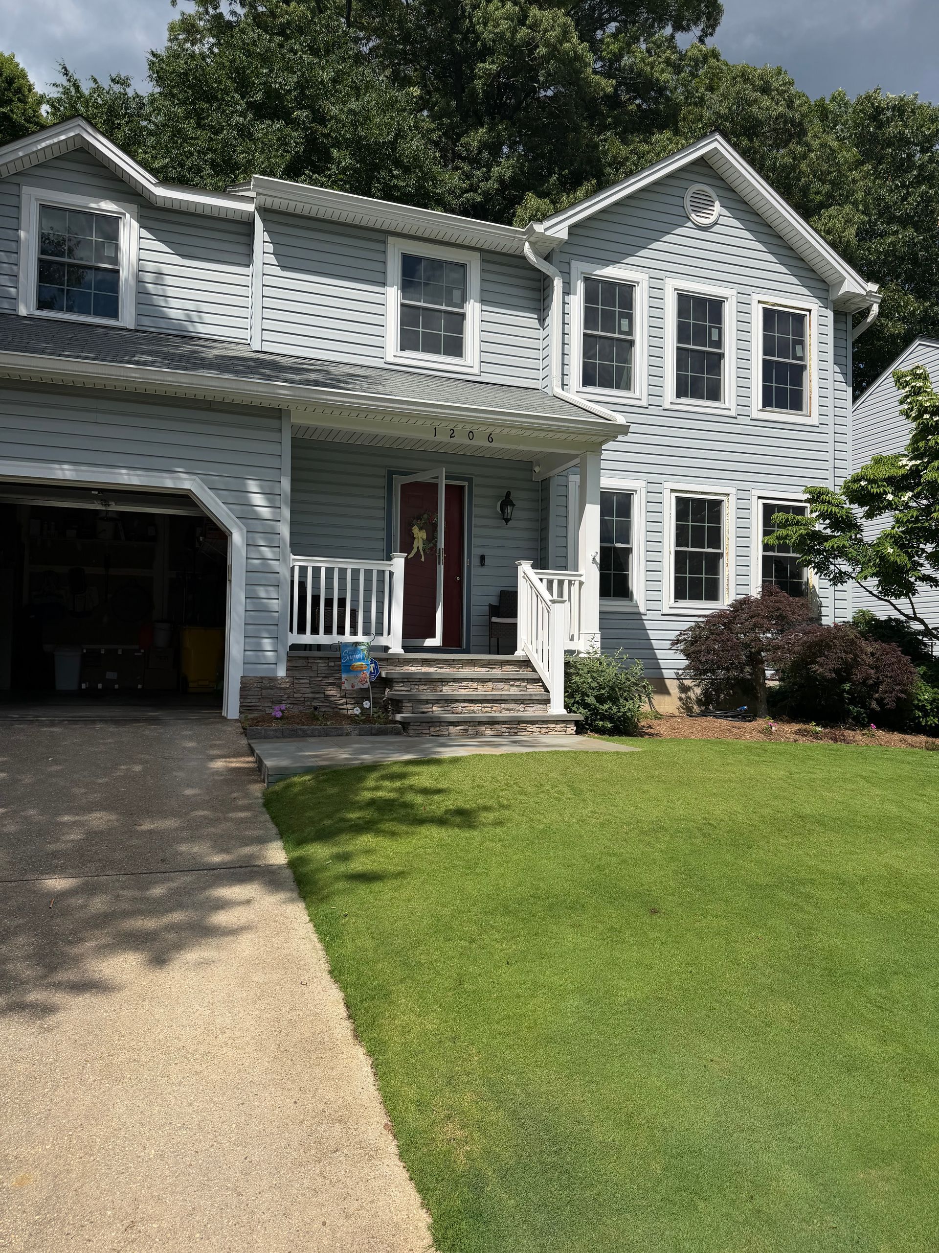 Two-story gray house with white trim, attached garage, and a green front lawn under sunny skies