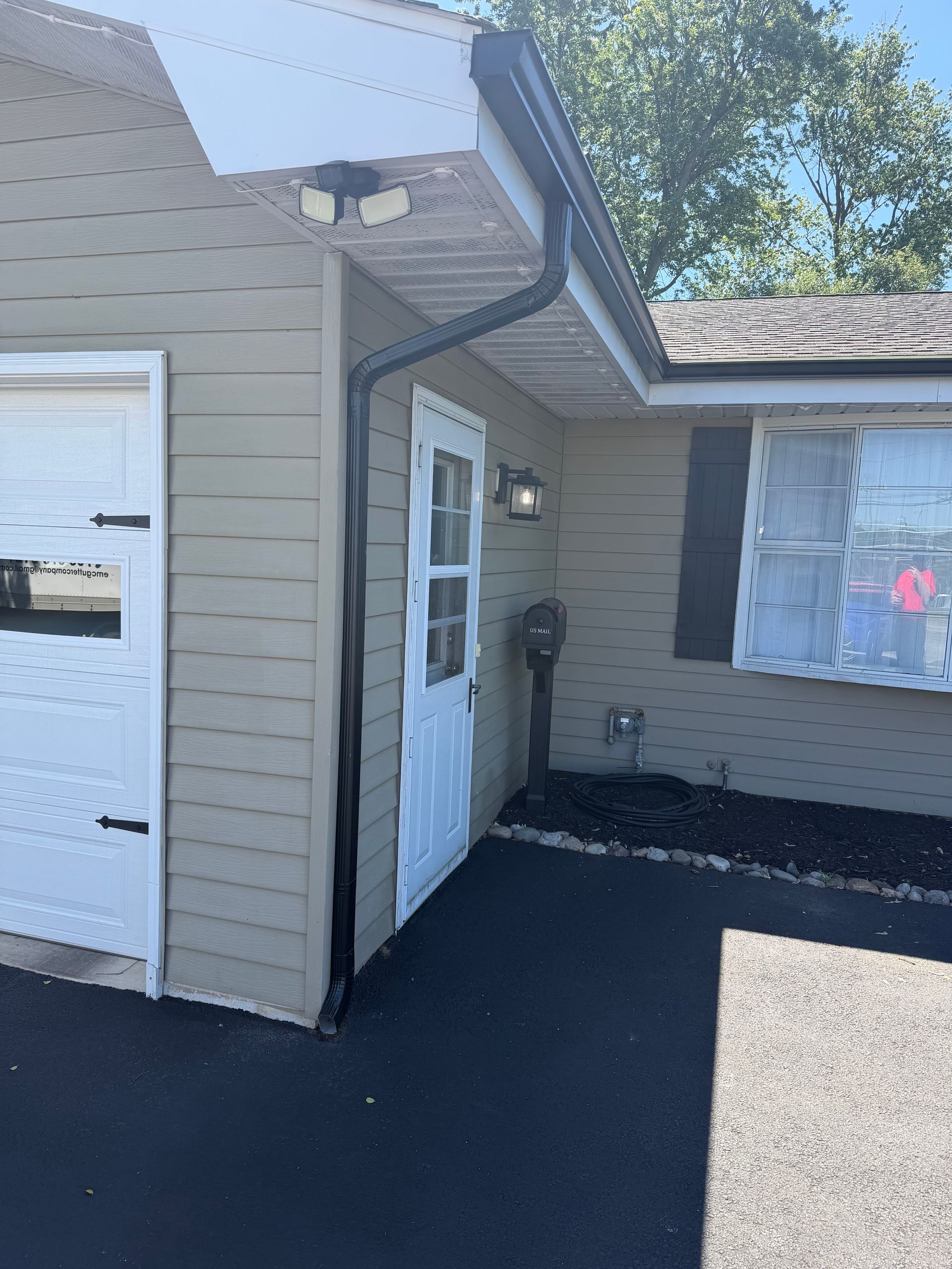 Exterior of a beige house with a white door, black pavement, and a boarded window.