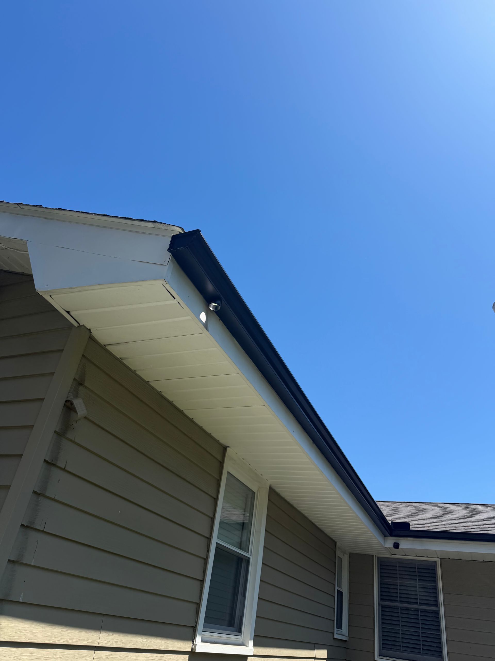 House roofline and siding under a clear blue sky, viewed from below