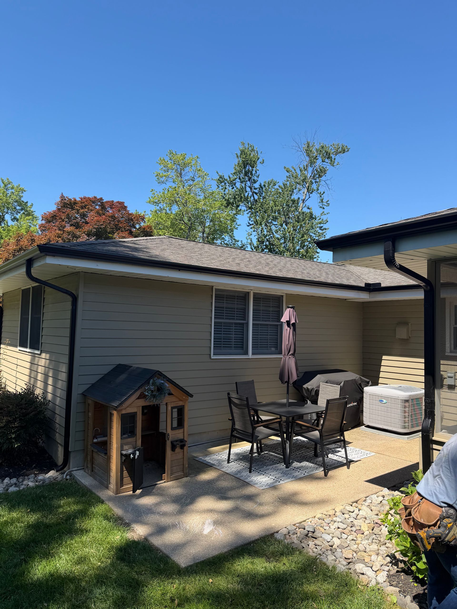 Backyard patio with table, chairs, a dog house, and a person standing near the house wall.