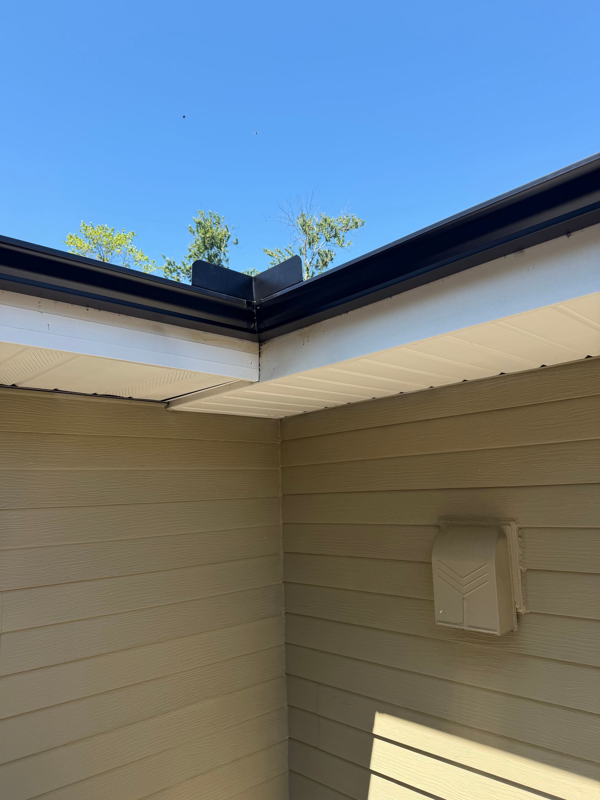Courtyard corner with beige siding, dark roof eaves, and a small wall-mounted box in sunlight