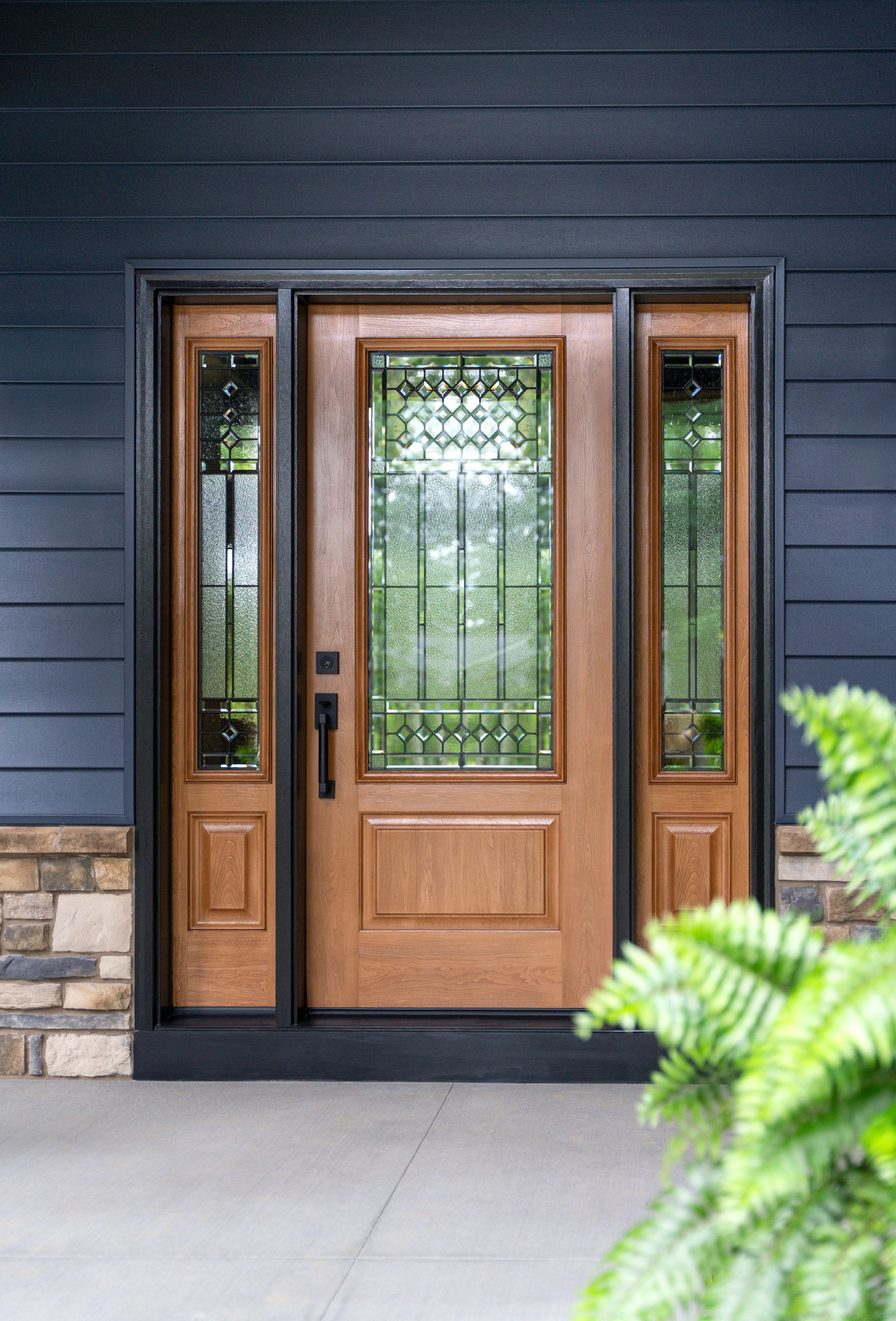Wooden front door with glass panels and side windows on a dark blue house exterior