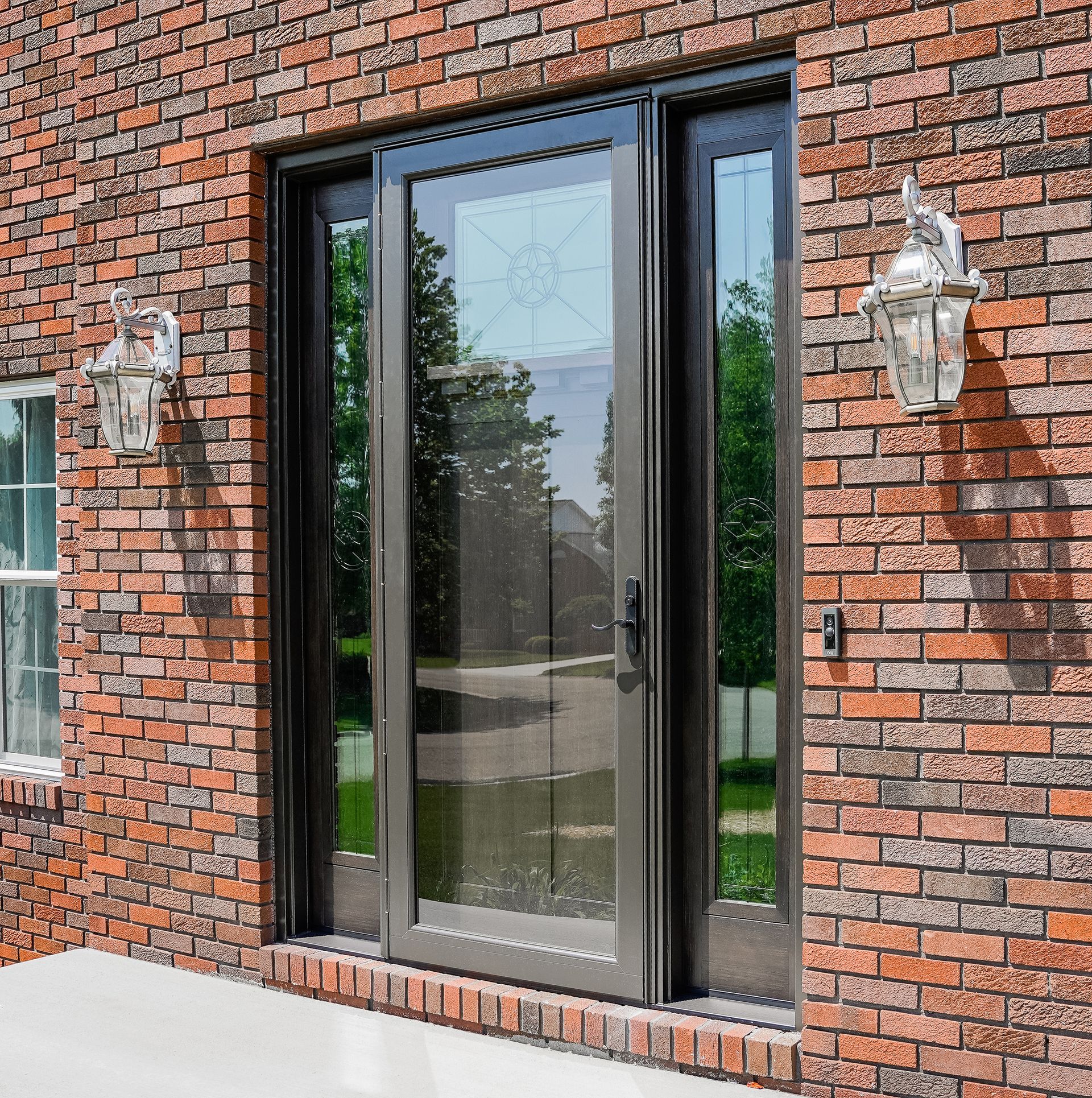 Brick exterior with a tall black-framed glass door and wall lanterns on either side