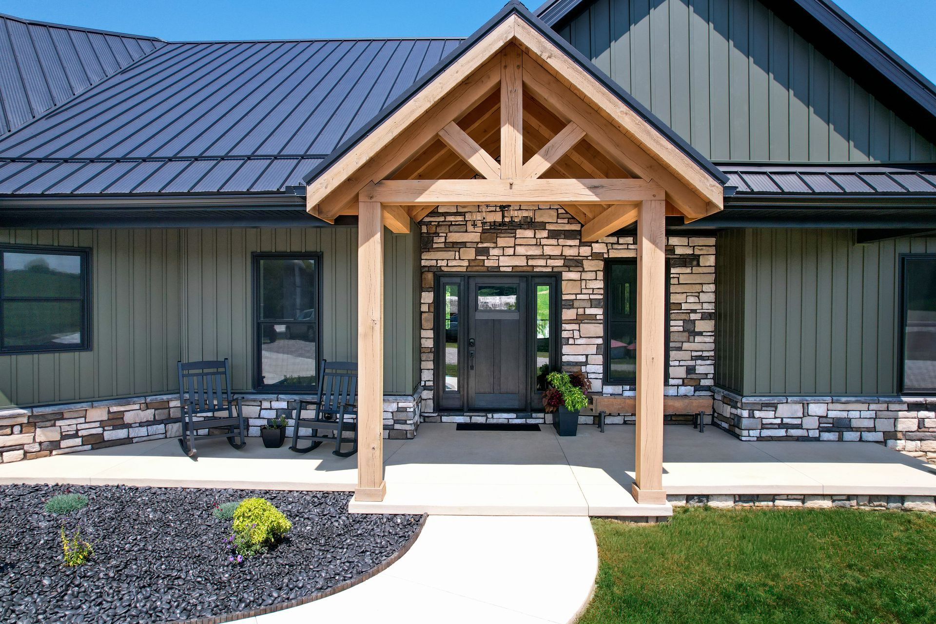 Front entrance of a modern house with a covered wooden porch, green siding, and a curved concrete walkway.