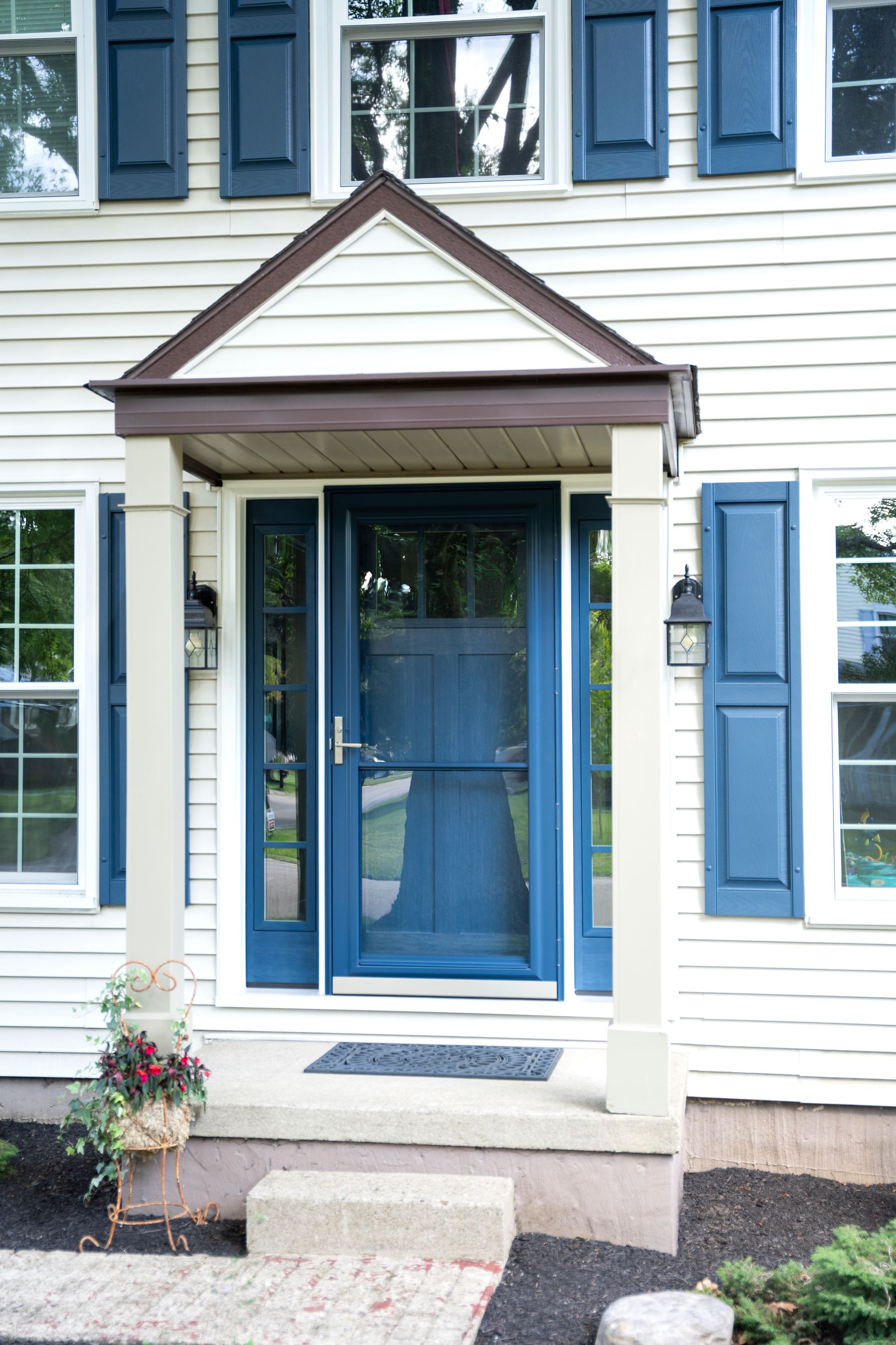 Front entrance of a white house with blue door and shutters, small porch, and steps leading up.