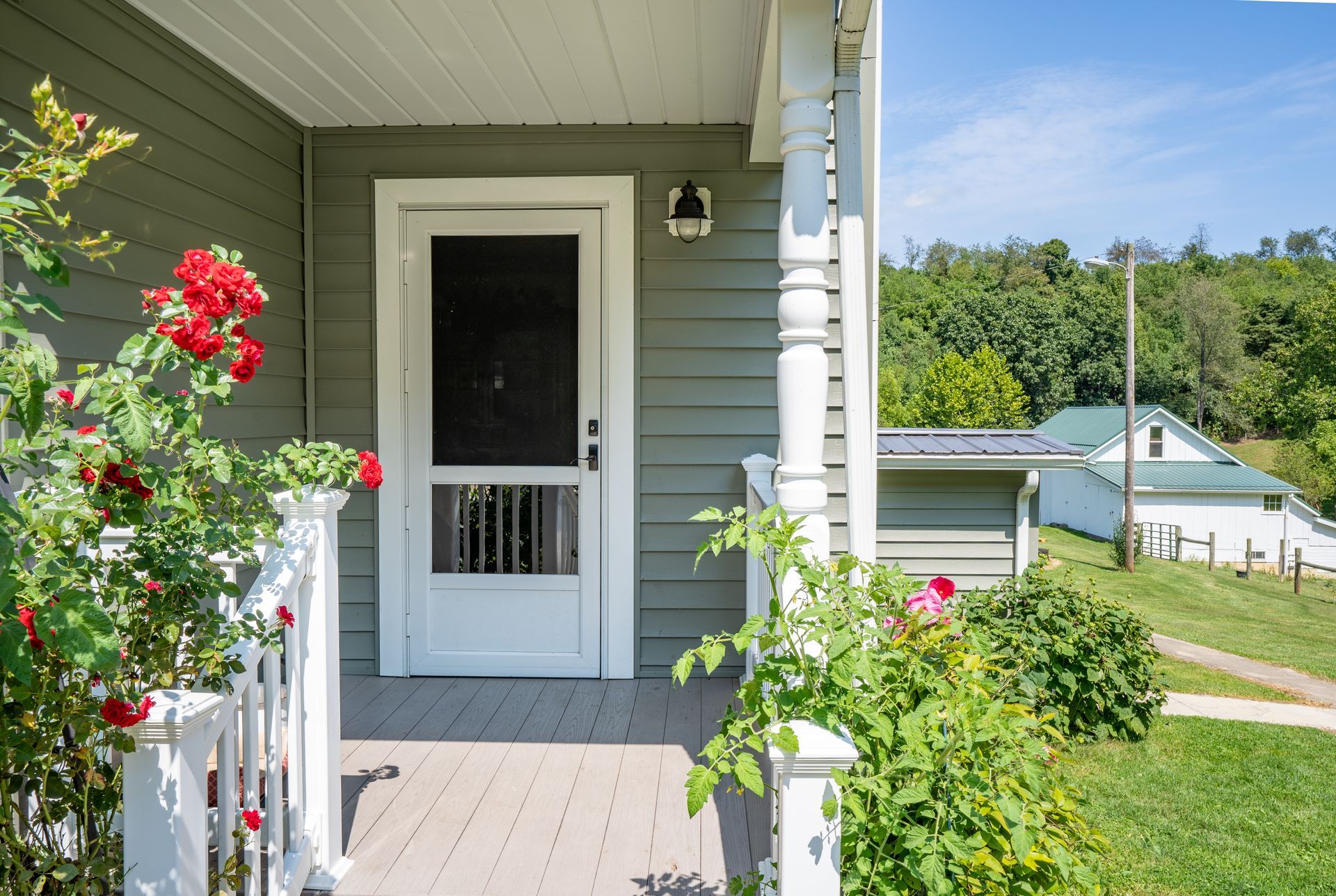 Front porch with white door, green siding, and red flowers overlooking a lakeside view