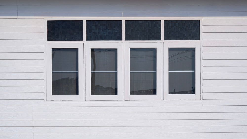 Four white-framed windows in a white horizontal siding wall with dark transom panes above