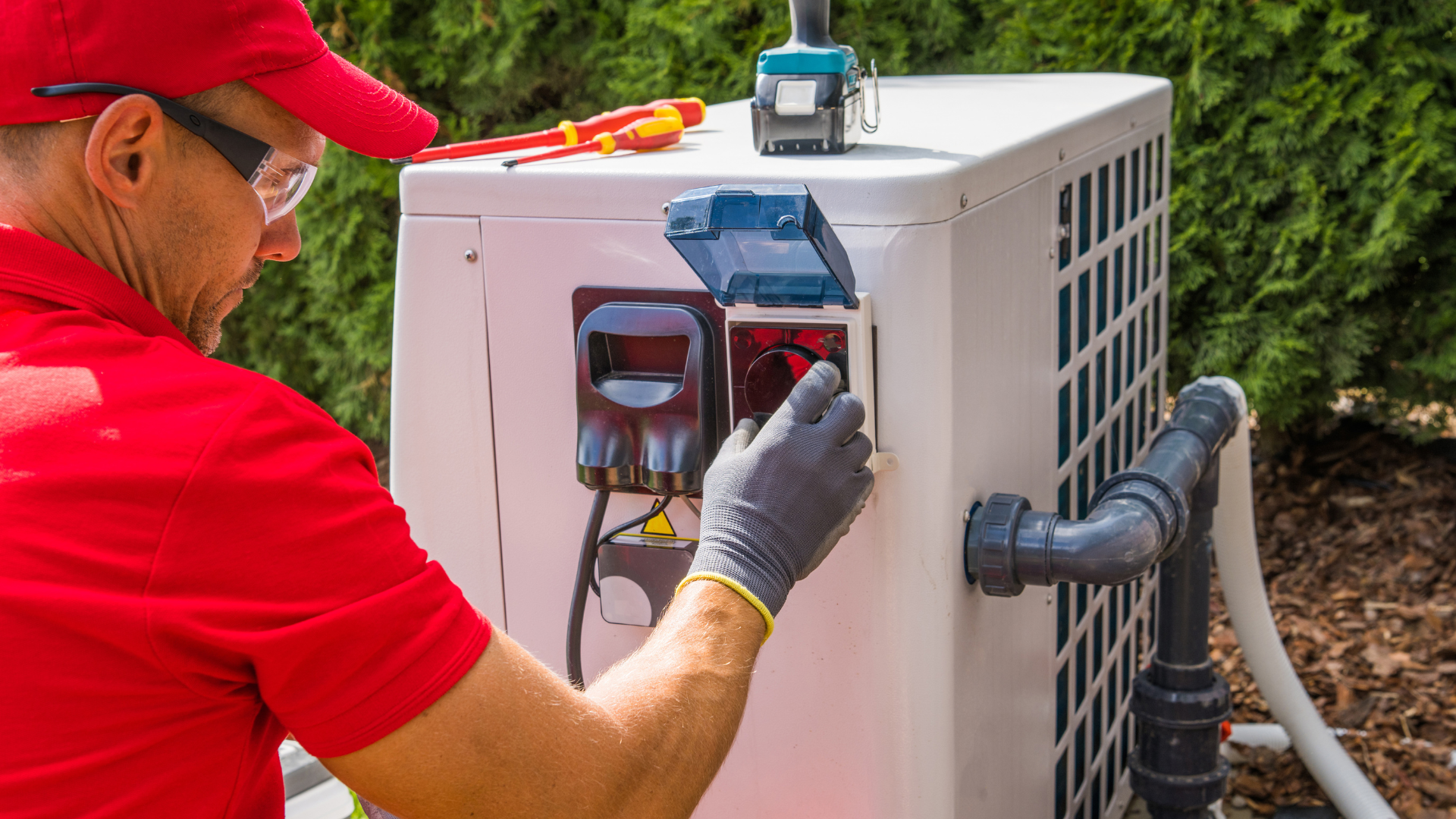 A man in a red shirt is working on a pool heater.