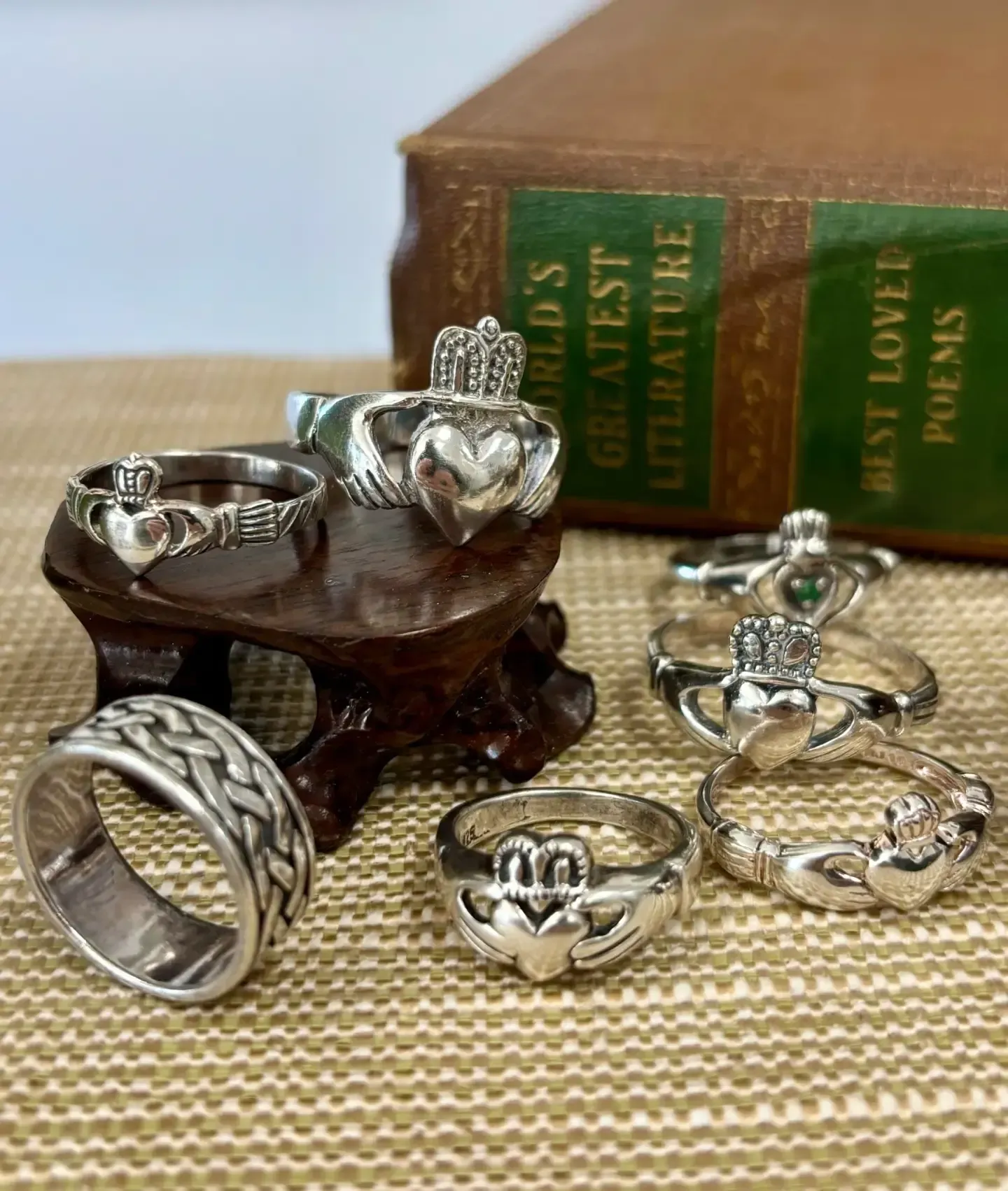 Six silver Claddagh rings and one braided band arranged on a table in front of a book titled