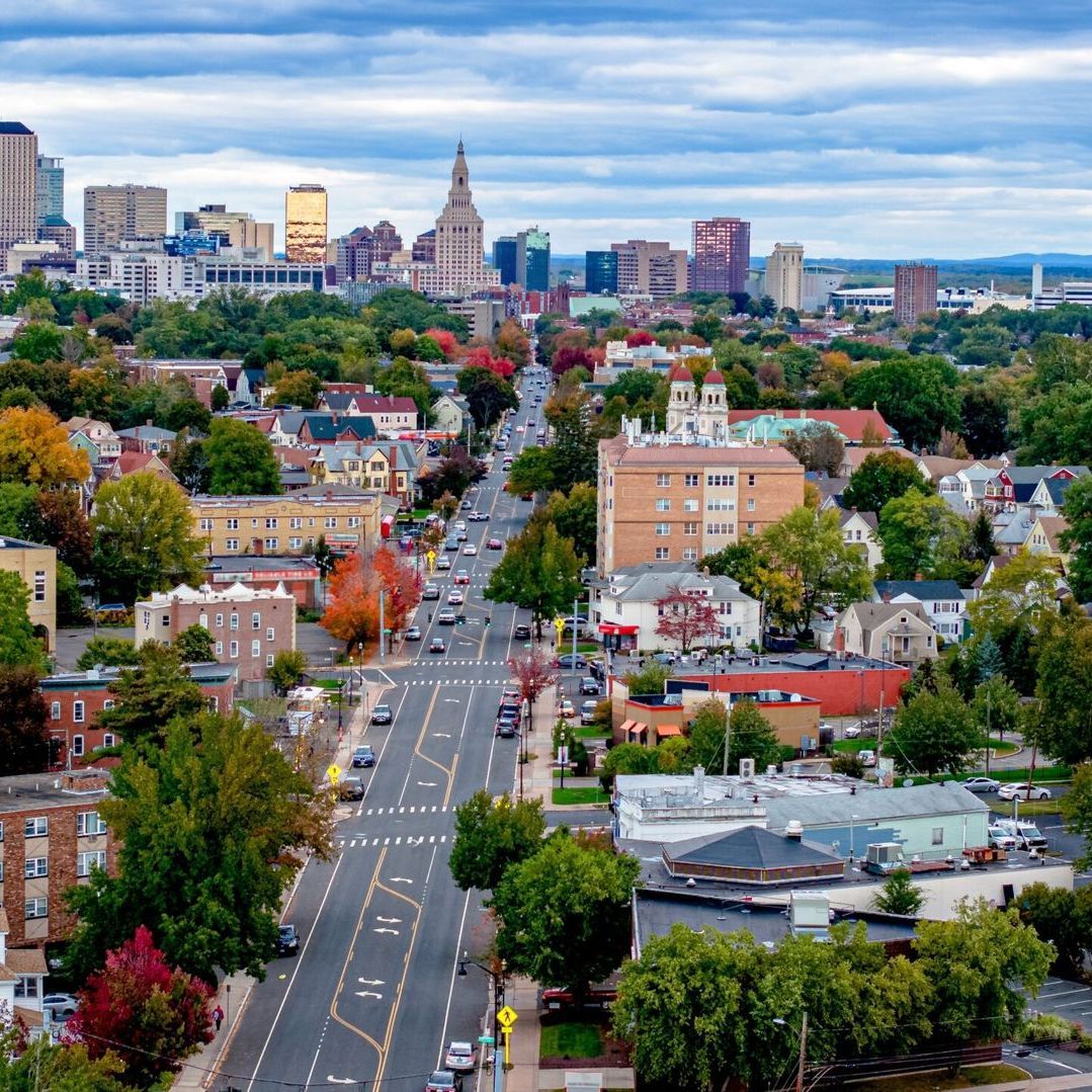 A small town in Connecticut with buildings and trees. Roads with cars on them.