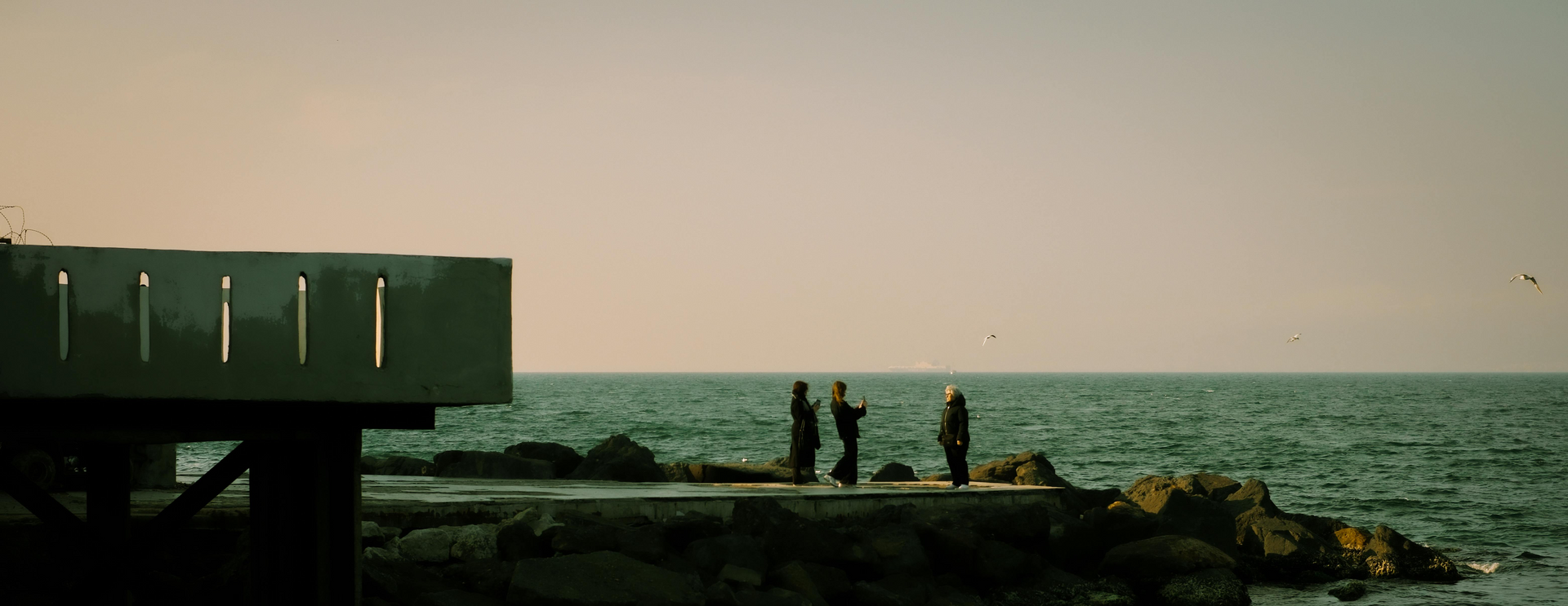 Three people on a pier on the shoreline in Connecticut. They are taking photos and making memories.