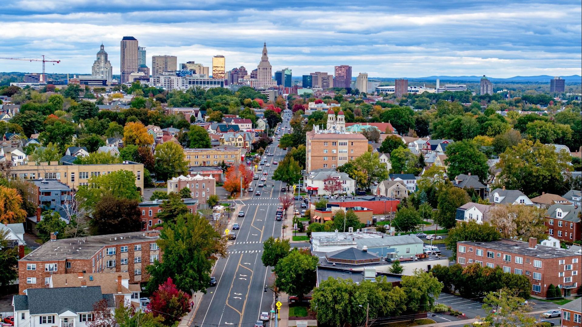 A small town in Connecticut with buildings, trees, and a road with cars driving on it.