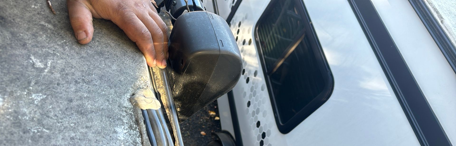 A man's hand on an RV roof and sealant that is coming off of the RV roof