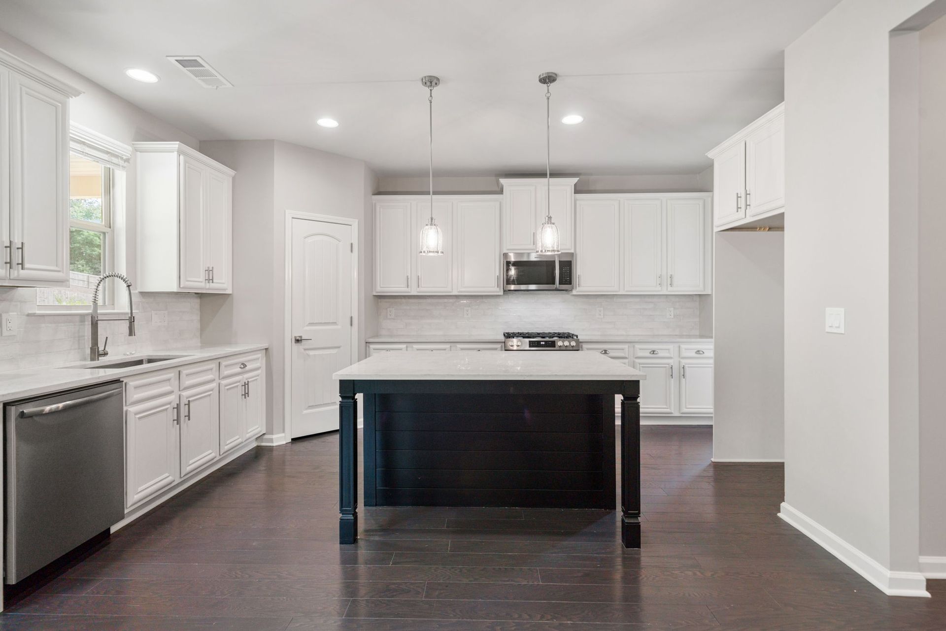 Modern white kitchen with dark wood island, stainless steel appliances, and dark hardwood floor.