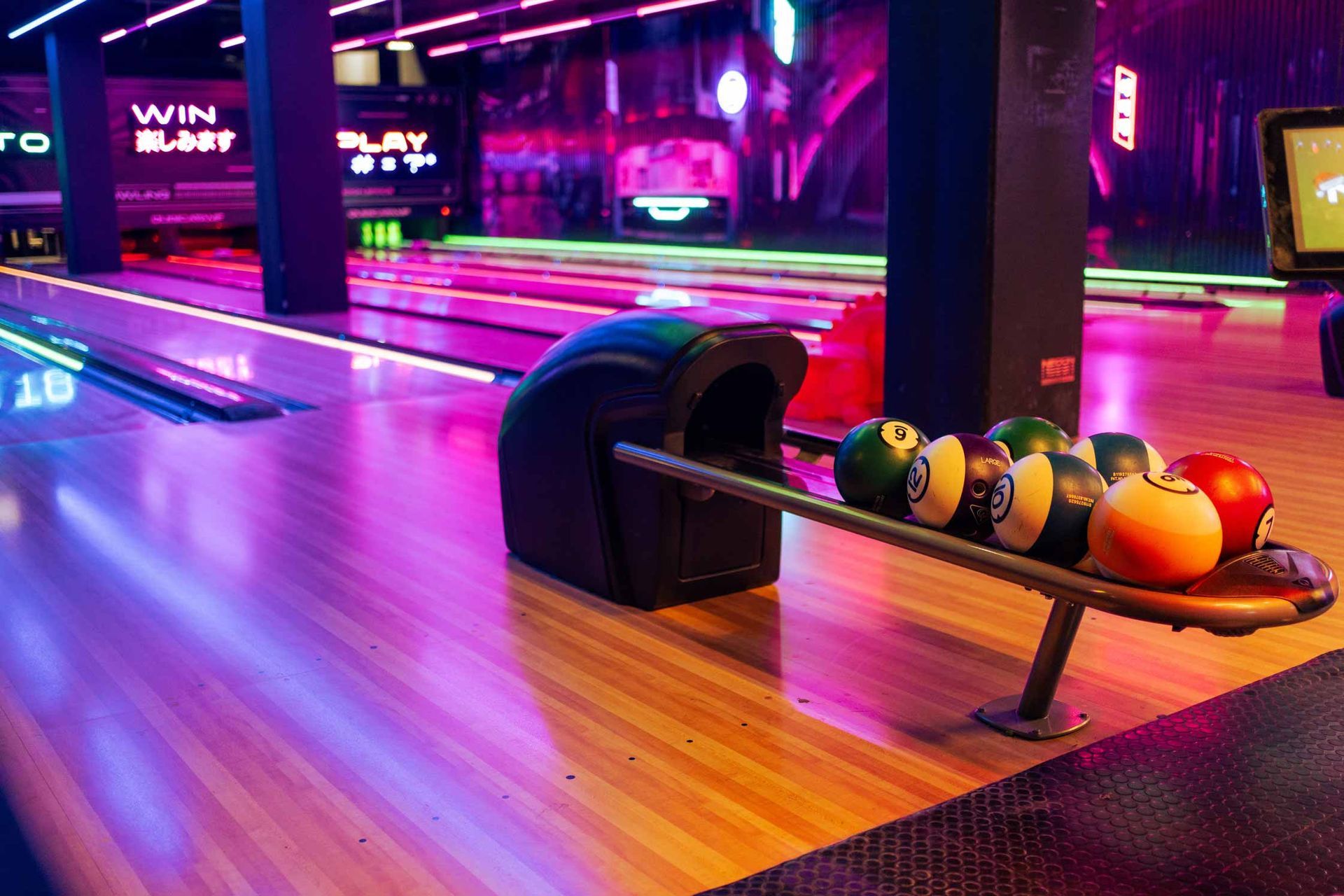Bowling lane with a ball rack in a neon-lit arcade alley
