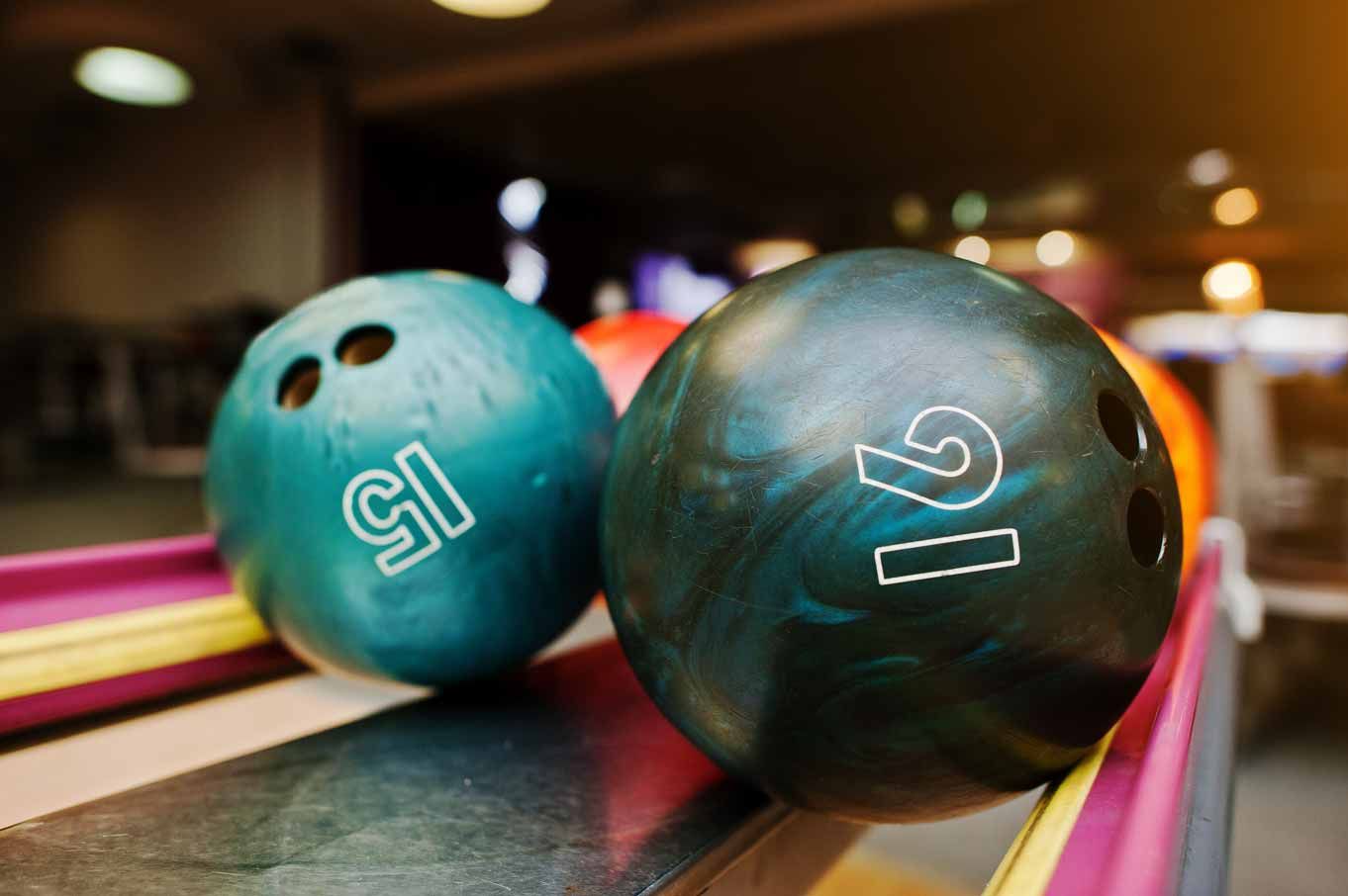 Two bowling balls, turquoise and black, resting on a bowling lane with pink rails.