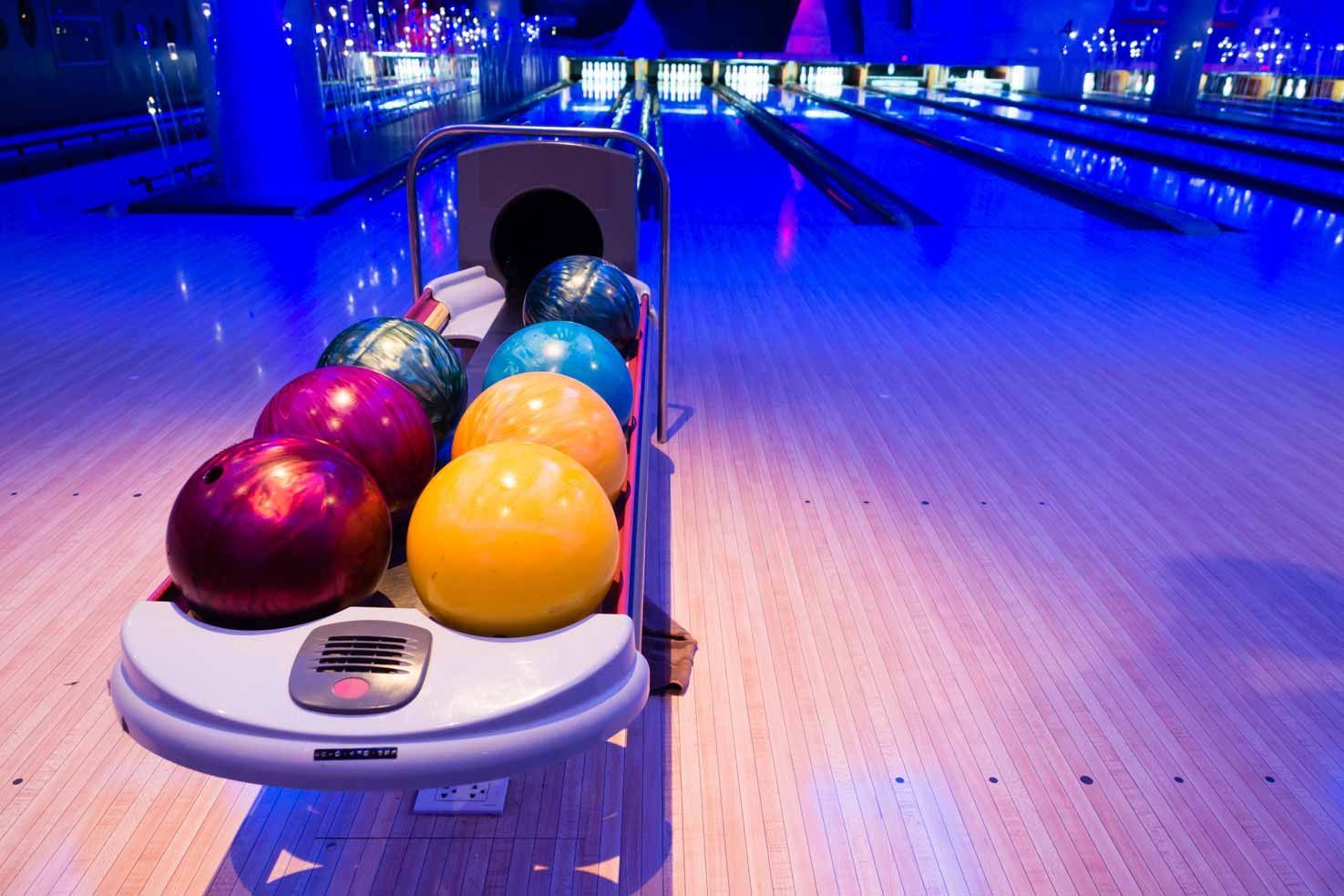Bowling balls on a return rack in a neon-lit bowling alley with lanes ahead