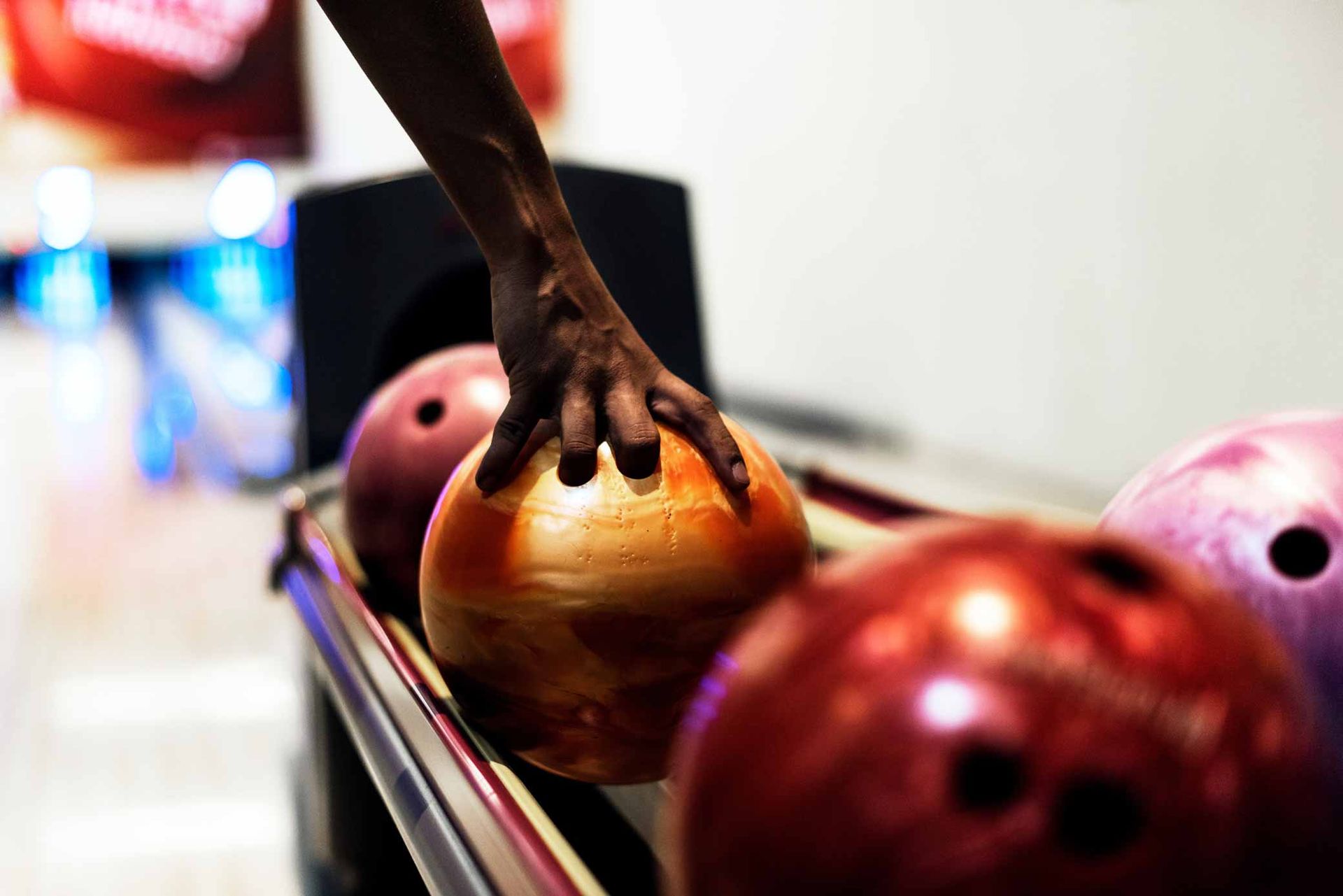 Hand reaching for a bowling ball on a rack at a bowling alley