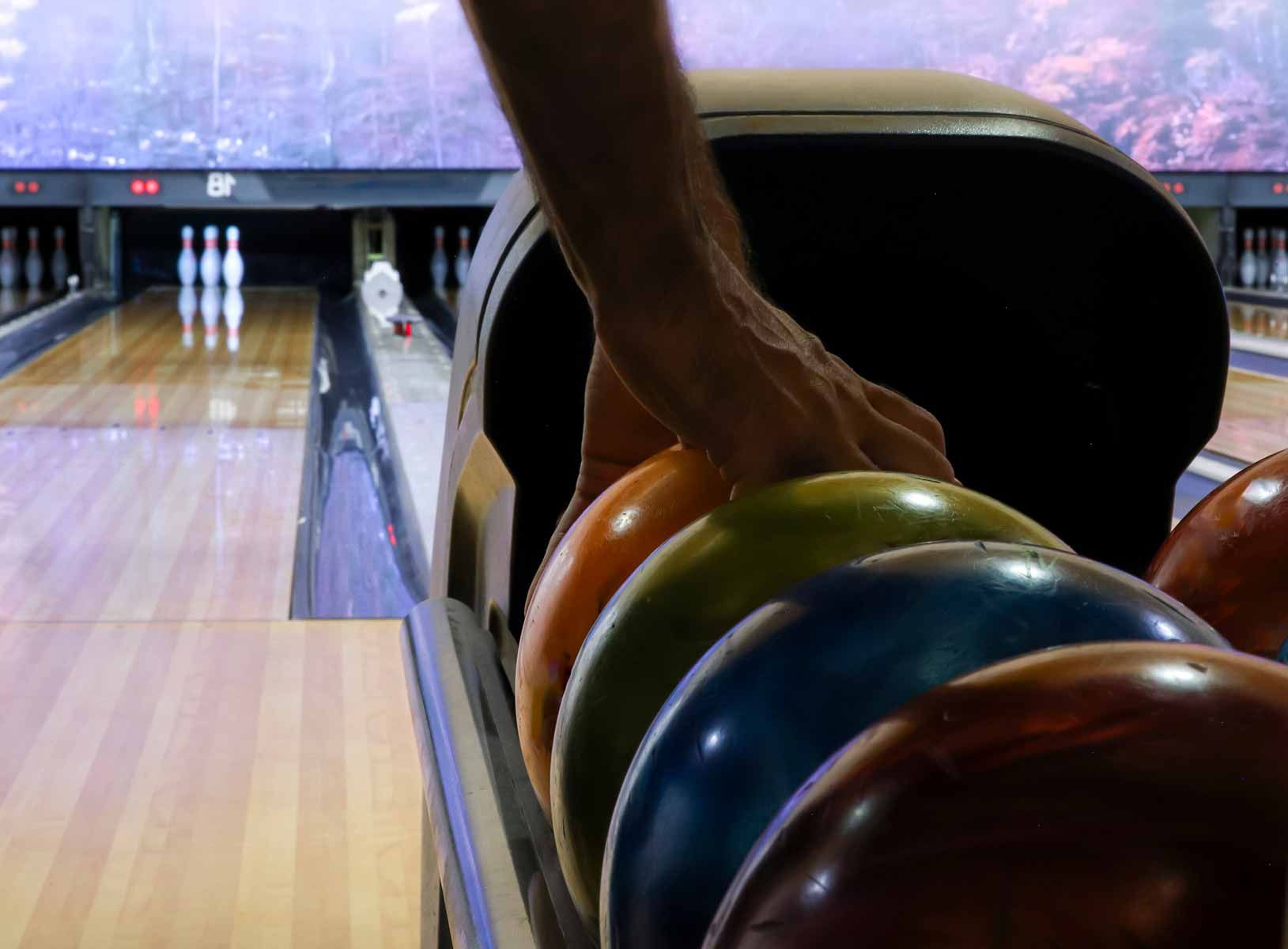 Hand placing a bowling ball in a rack at a bowling alley, with pins visible down the lane.