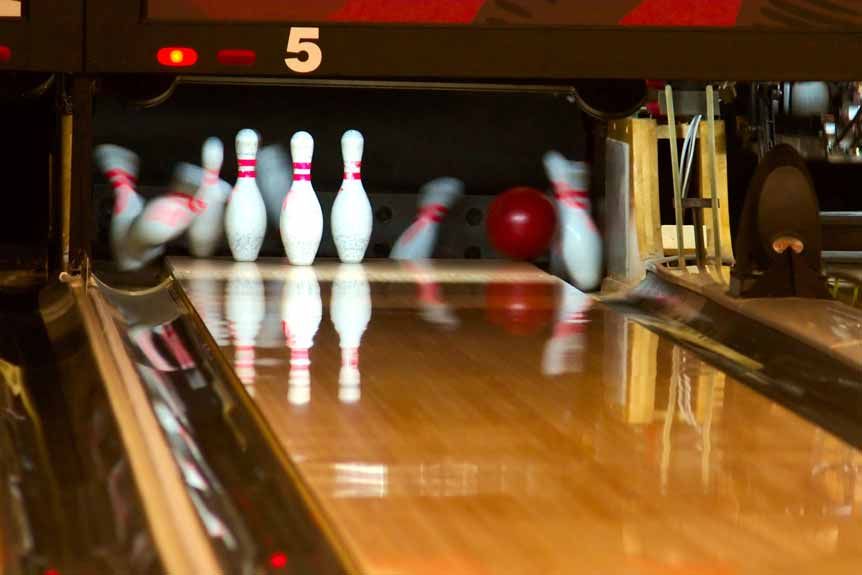 Bowling lane with pins set at the end as a red bowling ball rolls toward them