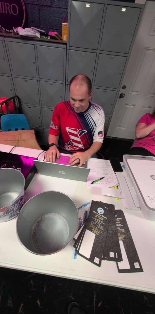 Person in a red shirt working at a table with papers and round gray props in a studio-like room.