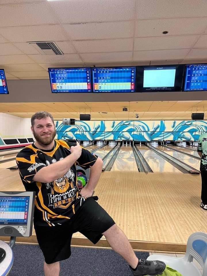 Bowling alley with a smiling bowler posing in front of the lanes and scoreboards