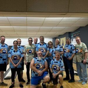 Group of people in matching blue jerseys posing indoors on a bowling alley lane