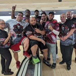 Group of people posing together in matching red, black, and gray jerseys at a bowling alley
