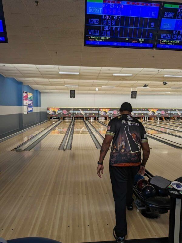 Bowling alley with a man walking toward the lanes beneath bright scoreboards