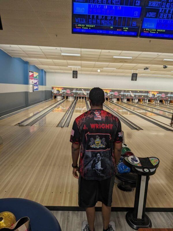 Bowling alley with a person standing at the lane, blue scoreboards overhead and a bowling ball rack nearby