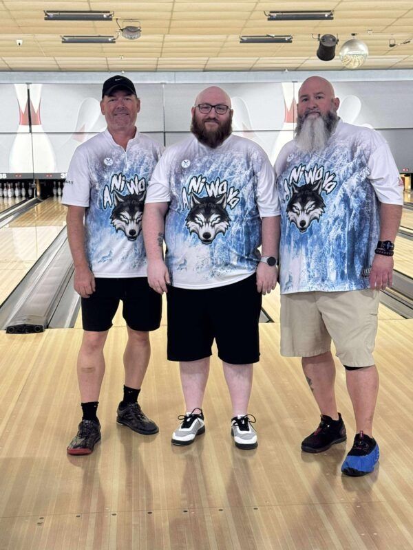 Three bowlers in matching shirts standing together in a bowling alley