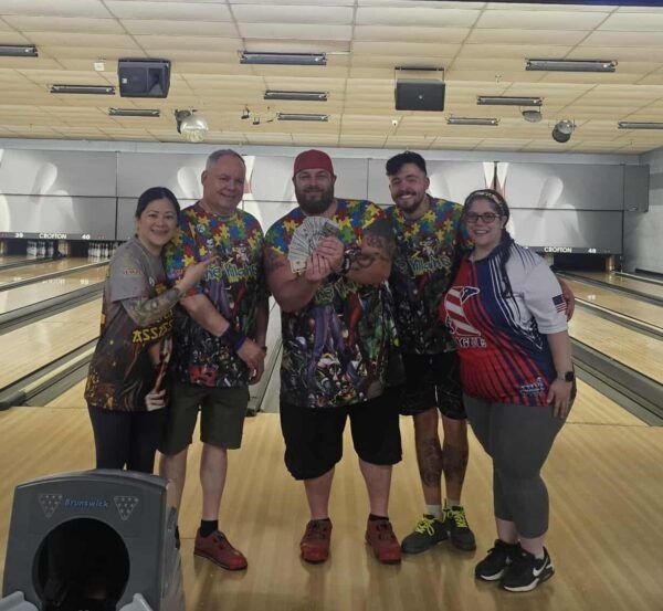 Five people posing together in a bowling alley, wearing colorful patterned shirts and smiling.