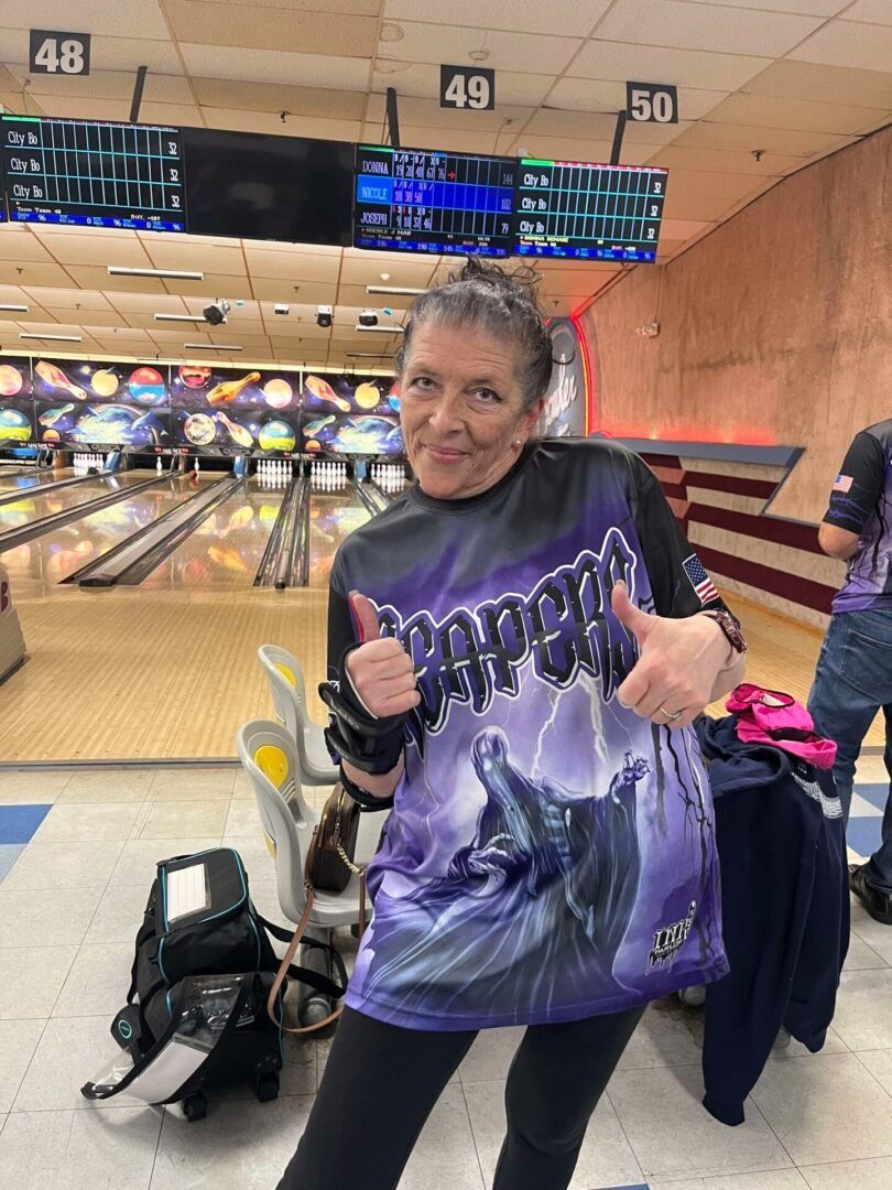 Bowling alley, person smiling and giving two thumbs up in a purple shirt near lane 49