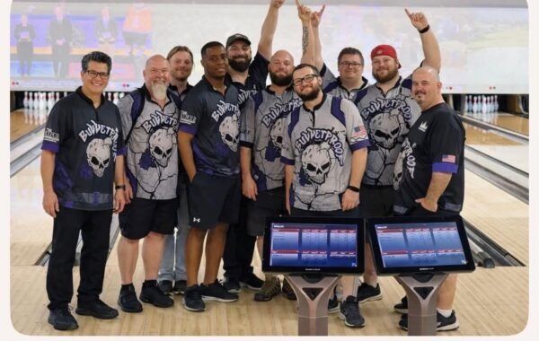 Bowling team posing in matching jerseys beside bowling lanes and scoring screens
