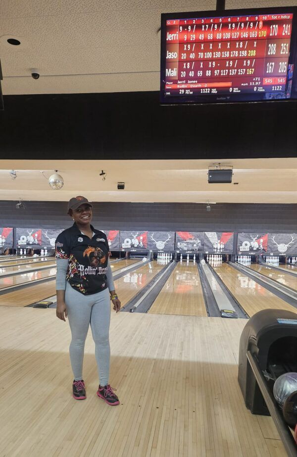 Person standing in a bowling alley in front of the lanes, with a scoring screen overhead.