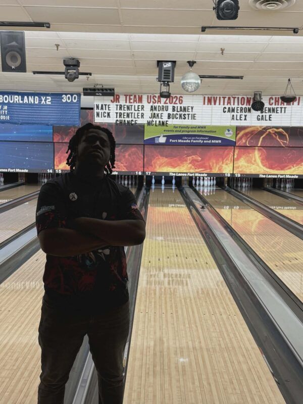 Person standing in a bowling alley, silhouetted in front of illuminated lanes and scoreboards.
