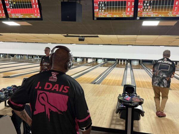 Bowling alley with two bowlers at the lanes, one in a pink-and-black shirt and headphones.