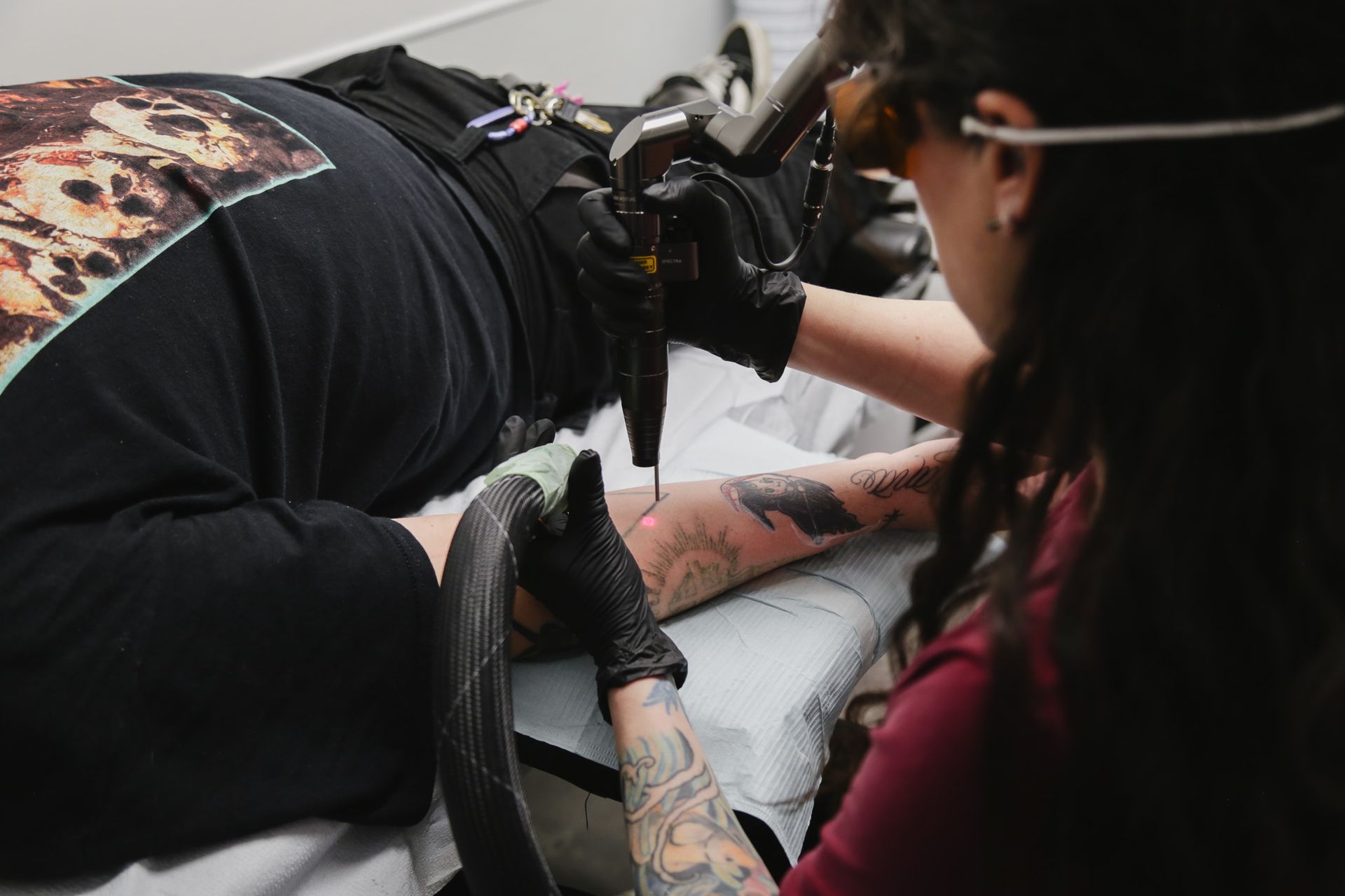 Tattoo removal technician working on a client and laser machine in a studio setting