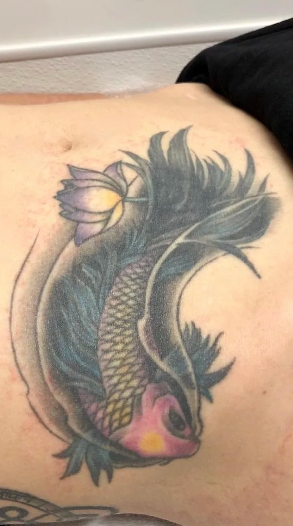 Colourful koi fish tattoo on the stomach, with a lotus flower and flowing black and blue fins.