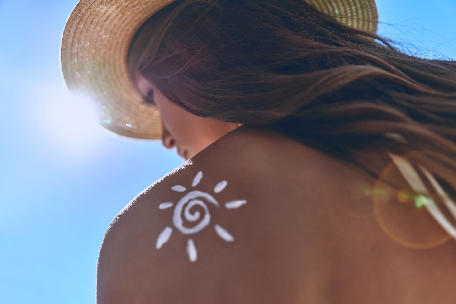 Woman in a straw hat with a white sun symbol tattoo removal on her sunlit shoulder