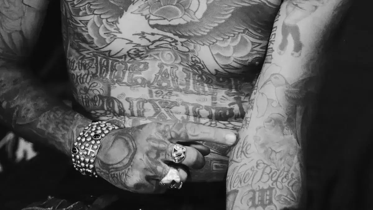 Person with heavily tattooed torso and arm, holding hand with ring and bracelet.