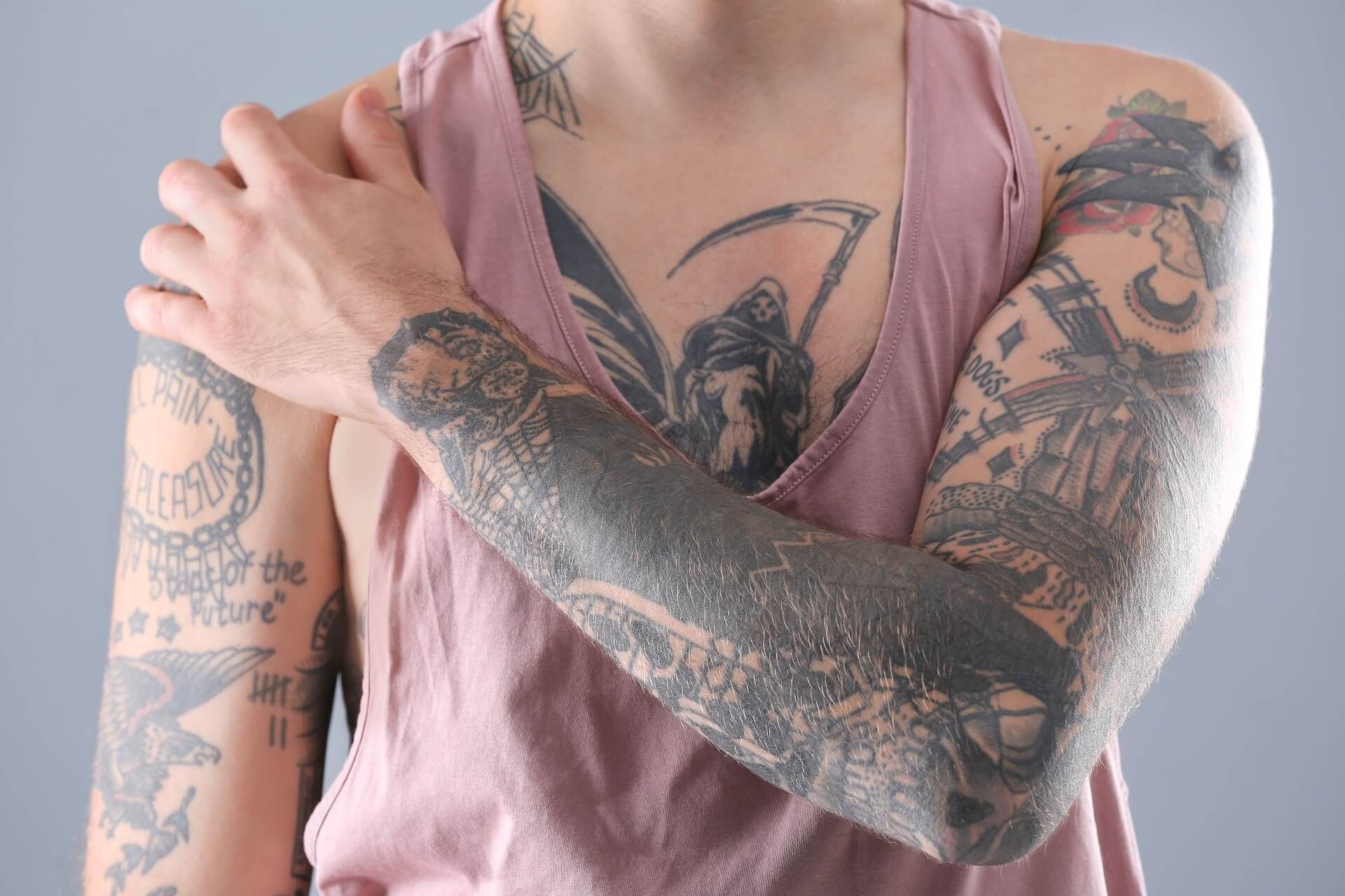 Tattooed person in a pink tank top crossing one arm over their scary tattoos