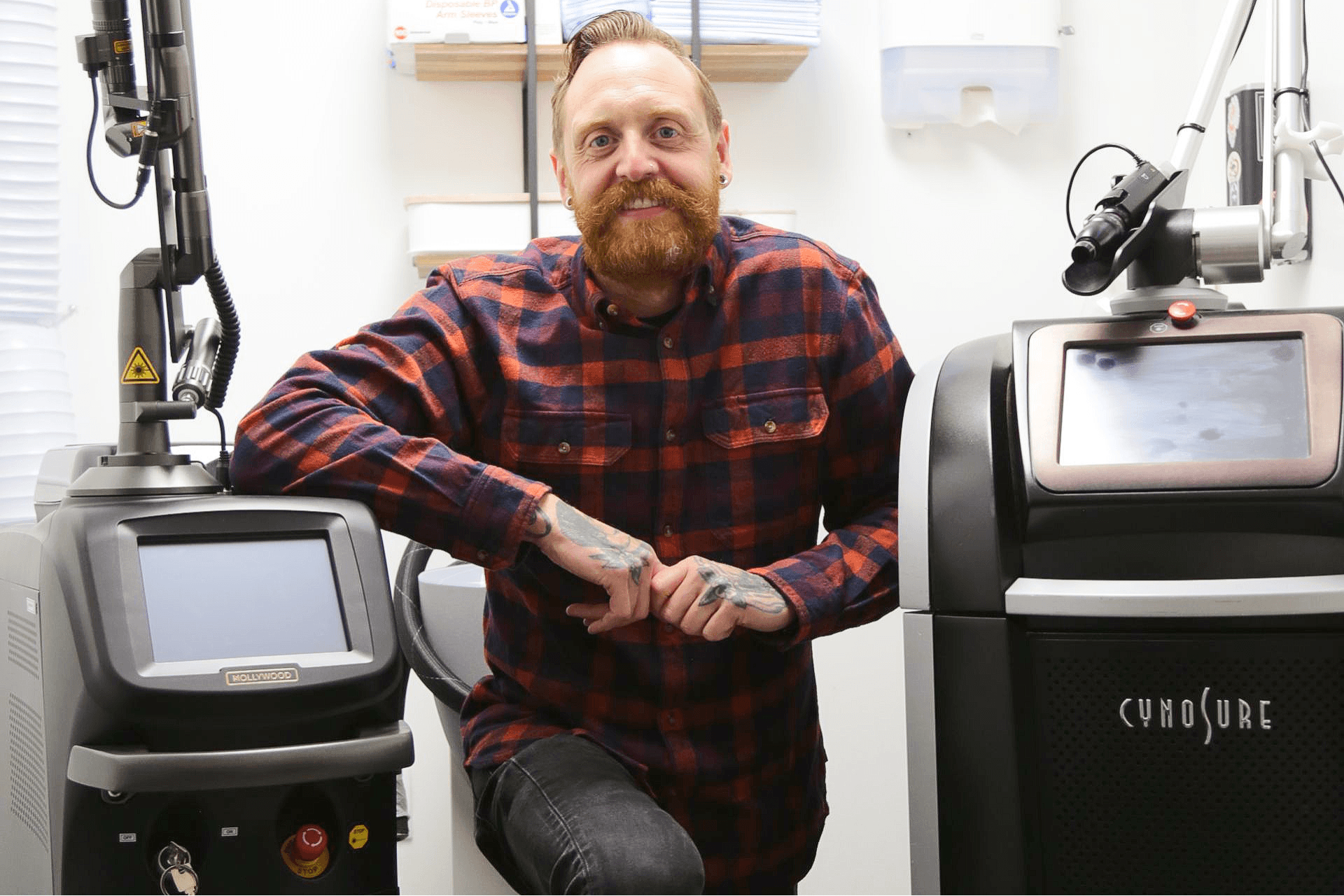 Man in red plaid shirt leaning between two laser engraving machines in a workshop